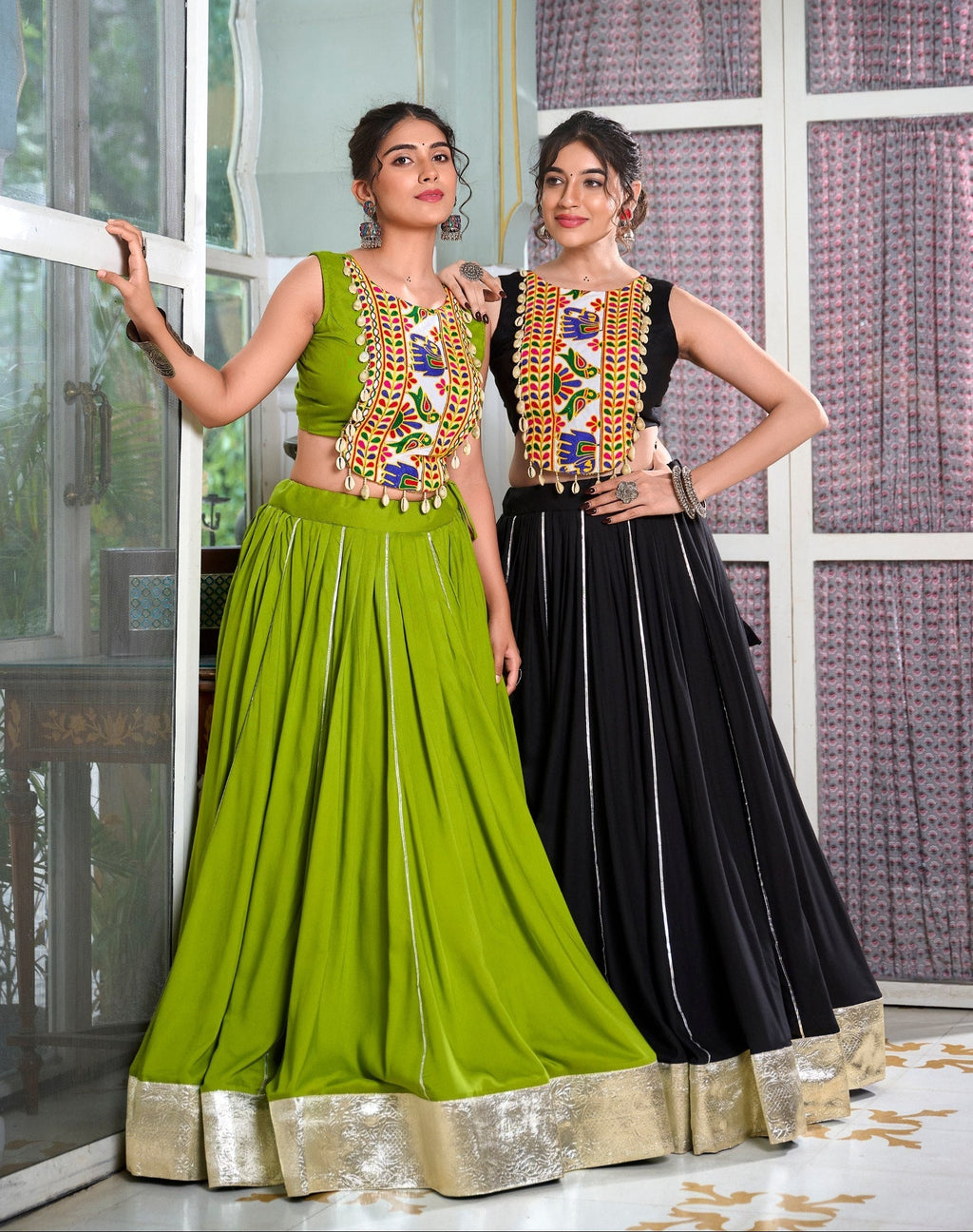 Two women wearing traditional outfits with colorful embellishments in a decorated room.